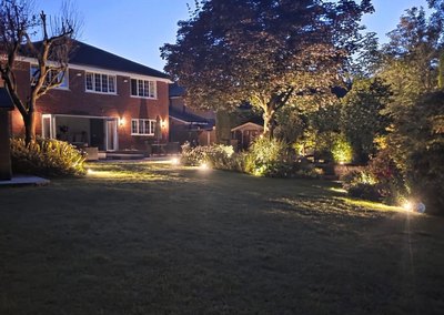 Garden lighting picking out the borders and trees of a lawned garden at dusk